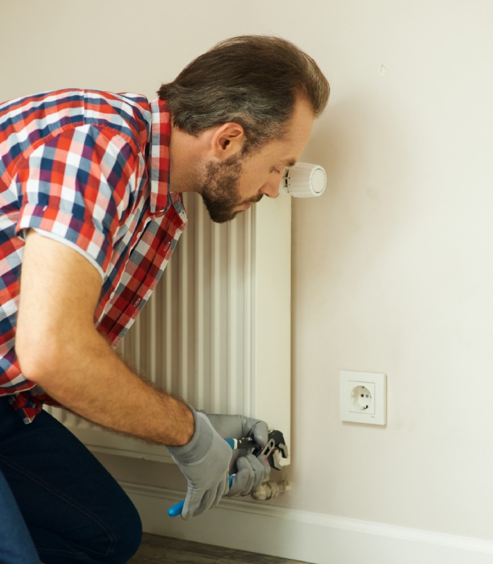 Technicien chauffagiste ajustant un radiateur mural lors d’une réparation de chauffage Griffon Multiservices